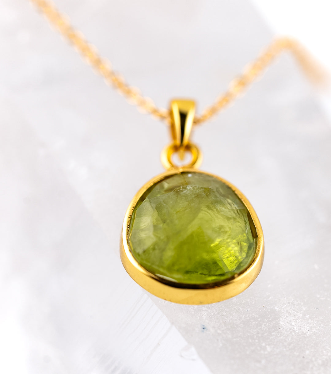 Gold pendant with a large peridot gemstone on a white background